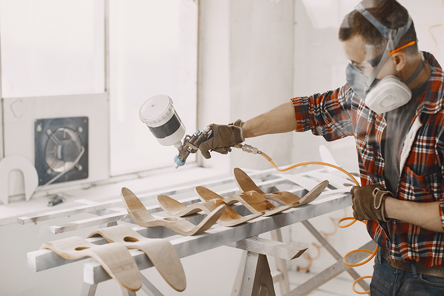Carpenter in his paint room spraying a piece of wood